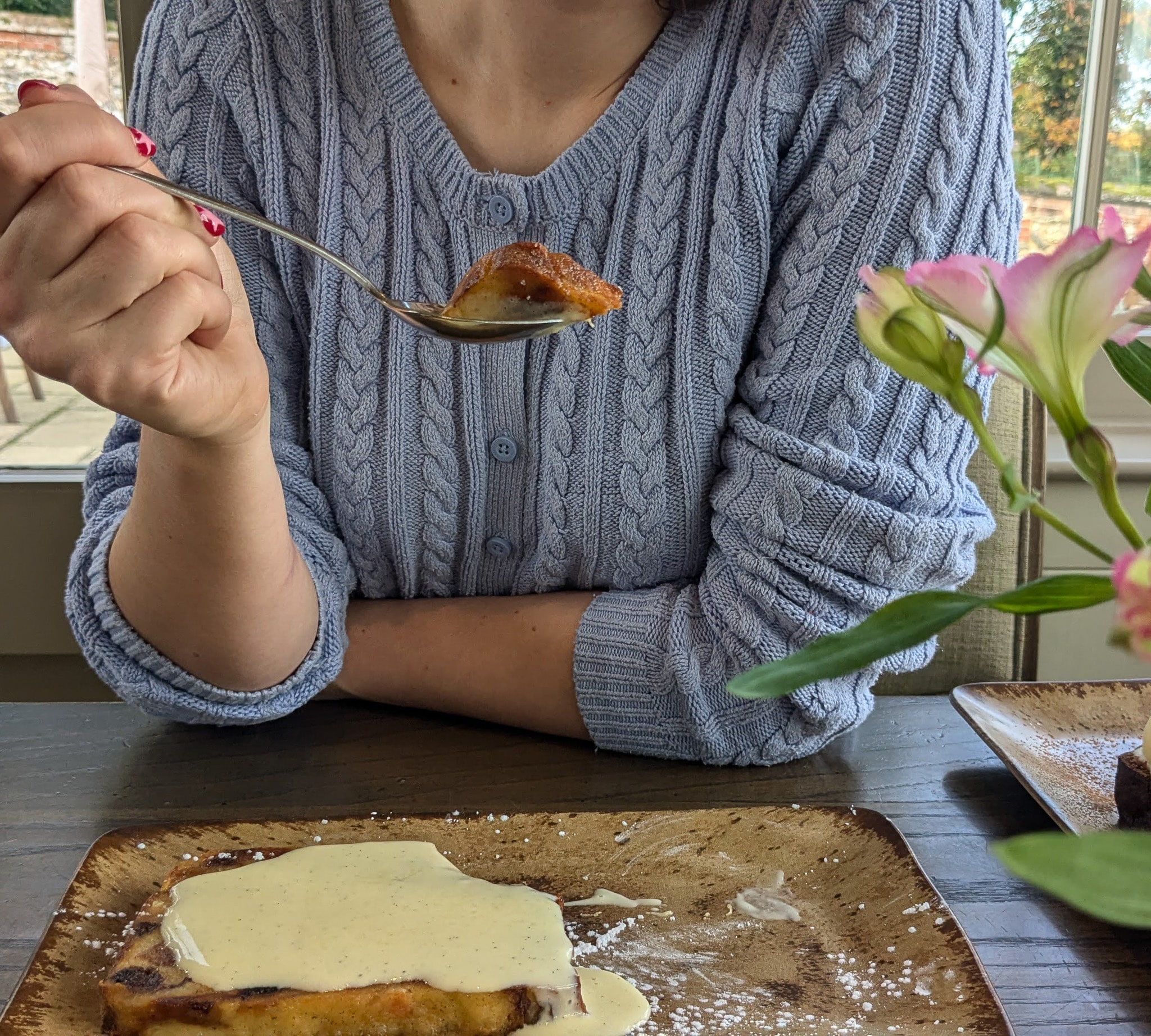 A woman holds a spoon of panettone bread and butter pudding over the plate, ready to eat.