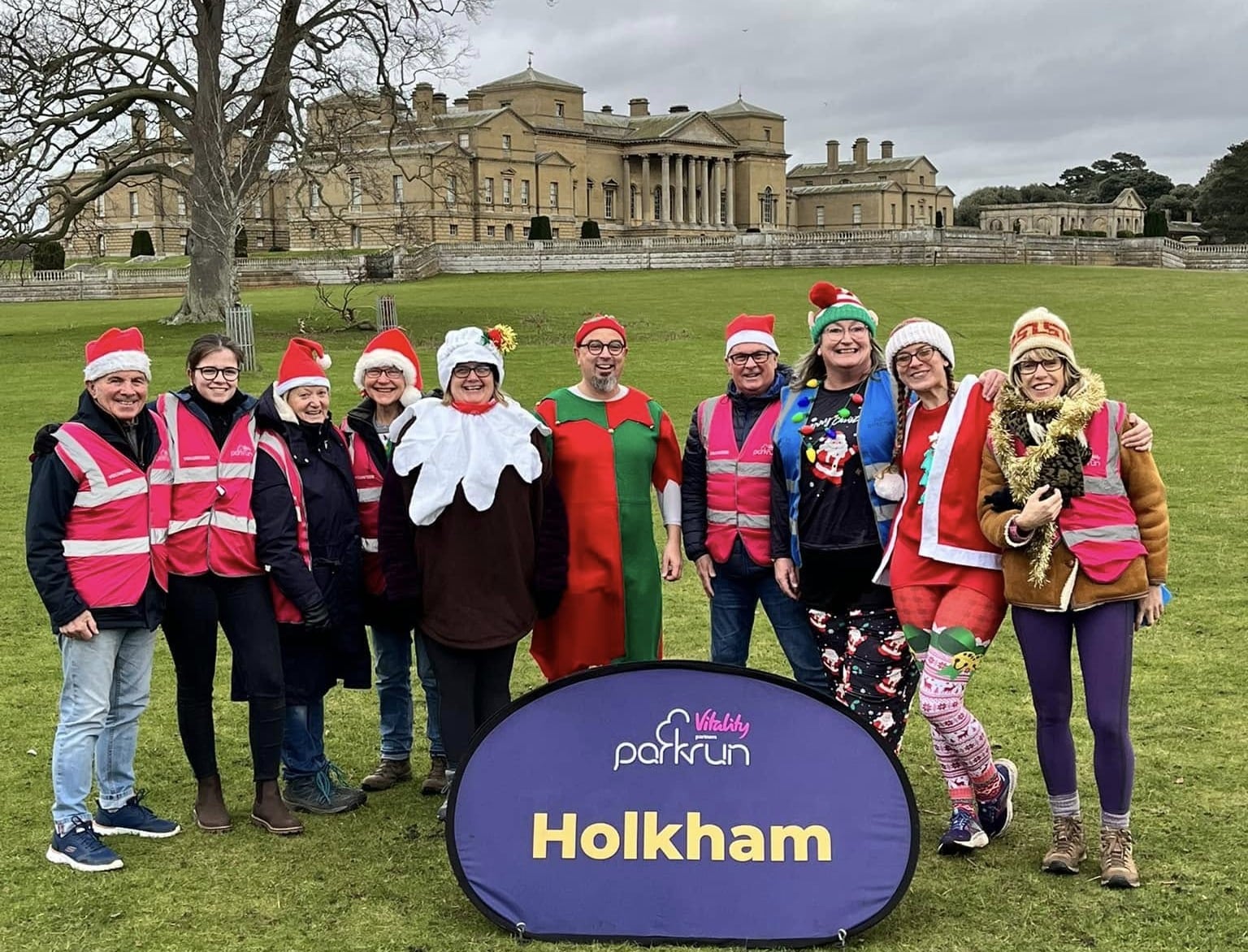 A group of parkrun volunteers dressed in Christmas outfits in front of Holkham Hall.