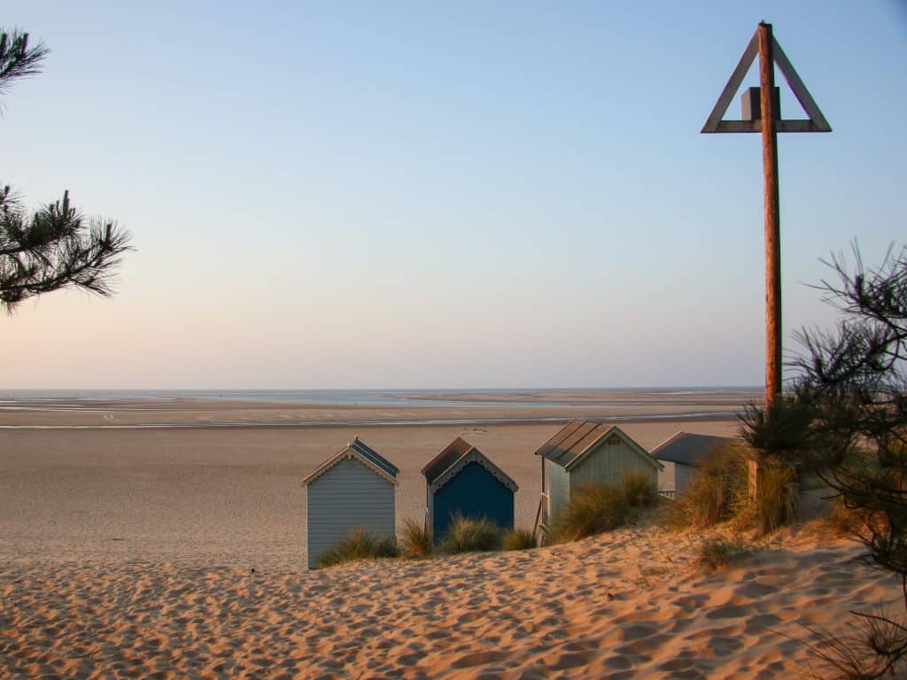 The backs of four beach huts on Wells Beach in Norfolk looking out to sea, taken from the dunes in the pine woods.