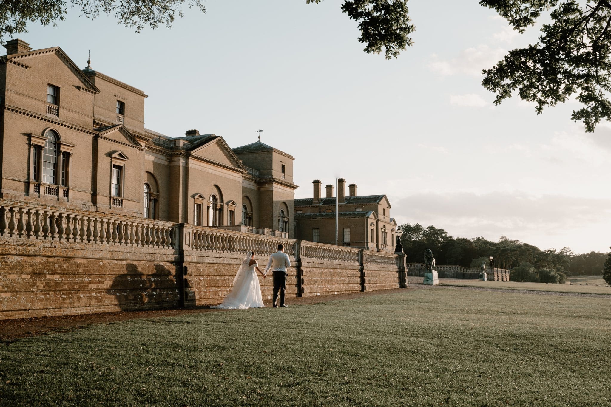 A bride and groom walk in front of the Palladian-style Holkham Hall, a stately home and wedding venue in North Norfolk.