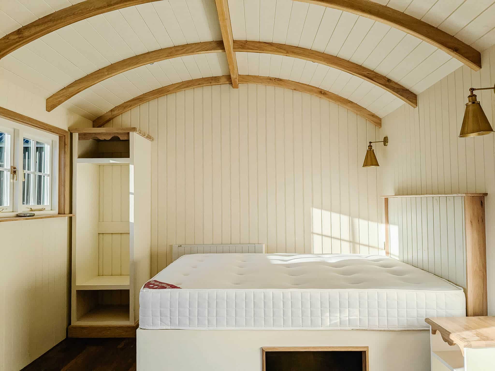 A light, bright interior photo of a shepherd hut bedroom area.